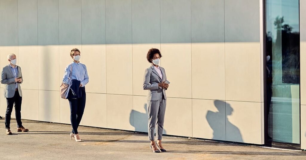 Administrar um condomínio e pessoas usando máscaras faciais, alinhadas e mantendo distanciamento social em frente a um prédio comercial.